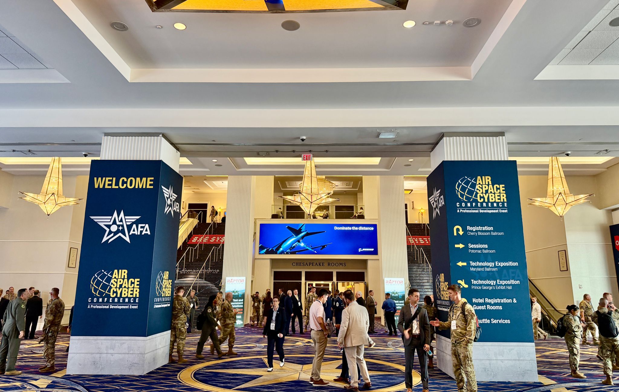 Attendees gather inside the Air, Space & Cyber Conference venue, with event signage and exhibit directions displayed in the main lobby.
